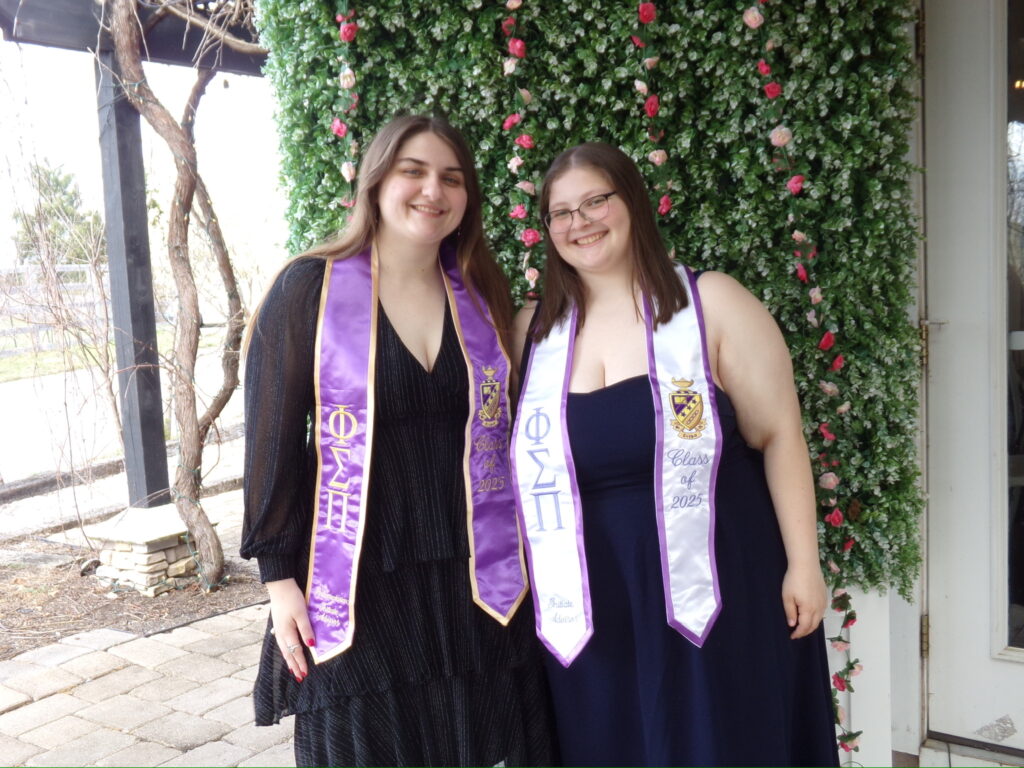 Two graduating Members stand together in Phi Sigma Pi stoles