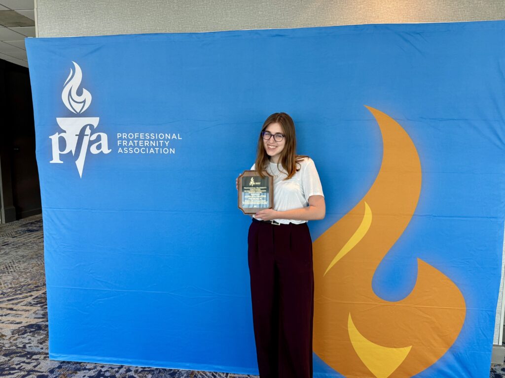 Alpha Eta Member stands with PFA award